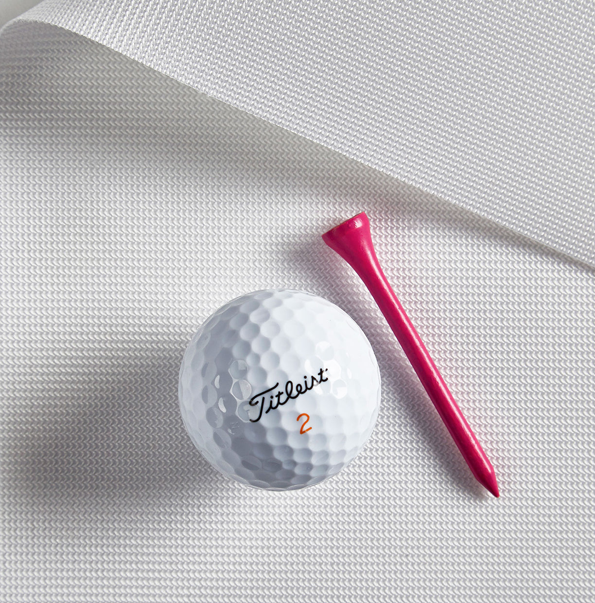 Titleist golf ball and pink tee on a white fabric background