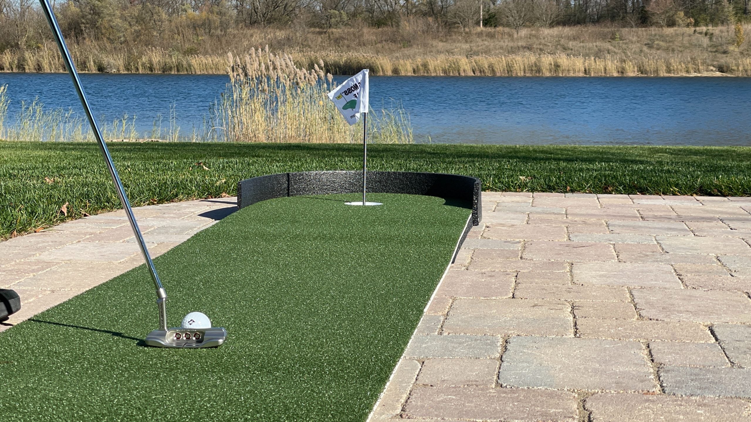 Golf putting green with flag and golf ball near a body of water