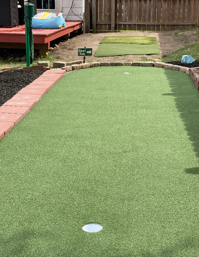 Miniature golf course with green grass and a white hole on a sunny day.