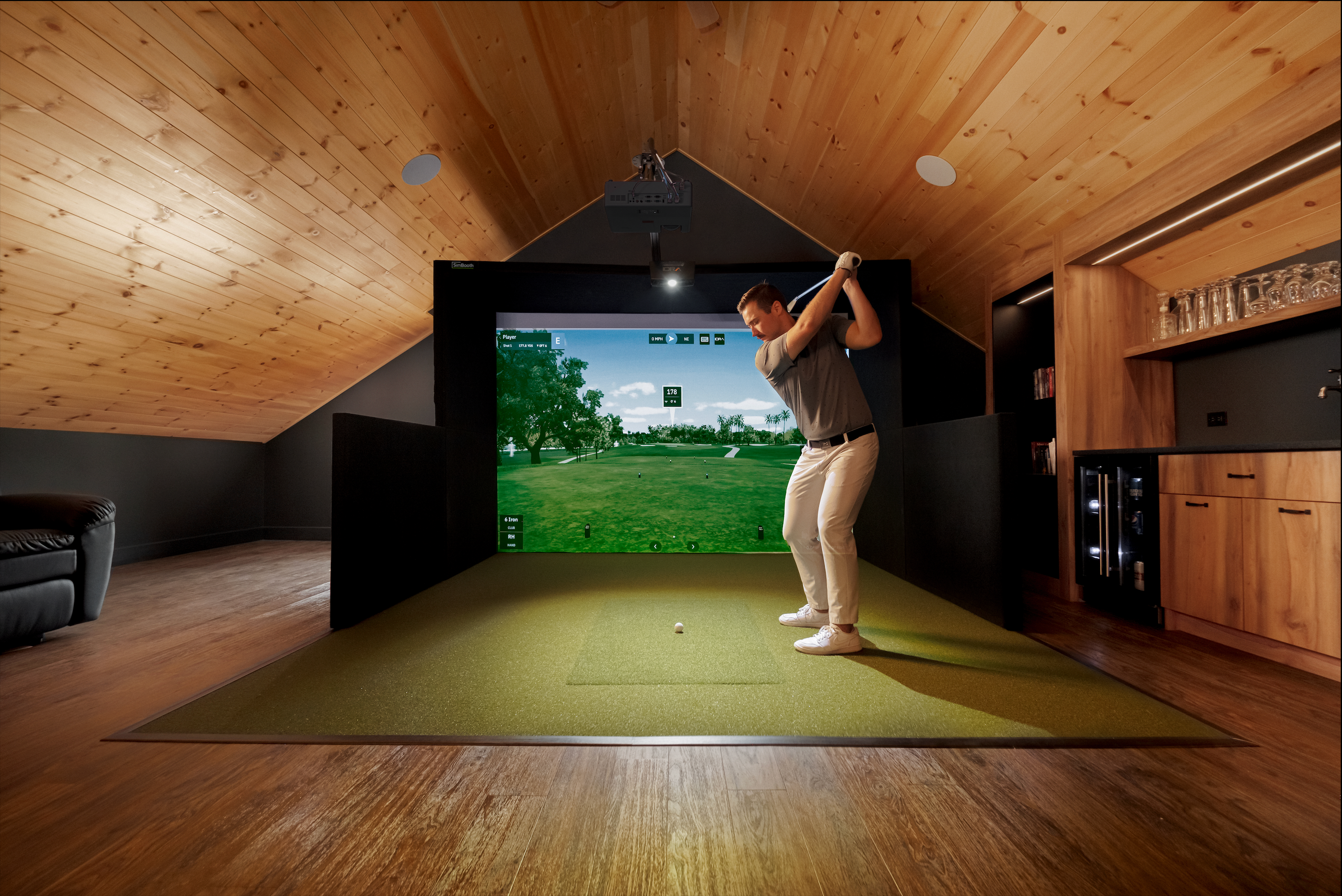 Man playing virtual golf in a home setup with a screen displaying a golf course.