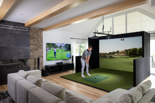 Man playing golf in a home simulator setup with a large screen and couch.